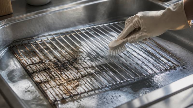 Grille de four encrassée trempant dans un évier et brossée avec une brosse souple