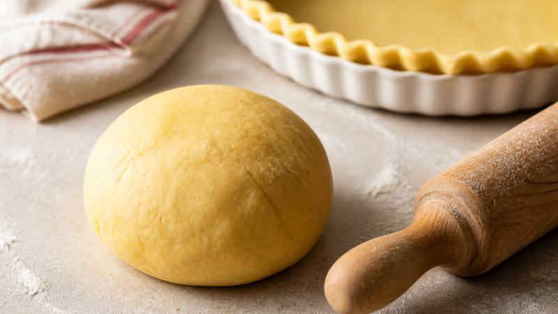 Boule de pâte brisée maison avec un rouleau et un moule à tarte