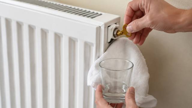 Purge d’un radiateur blanc avec une clé de purge, un chiffon et un verre
